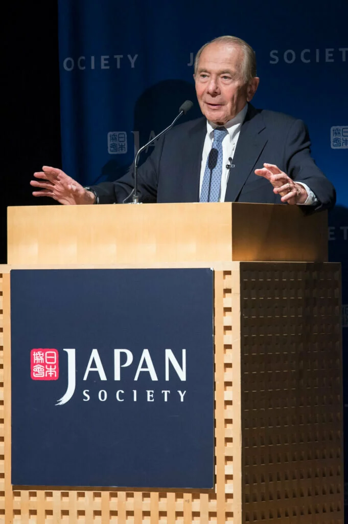 Mr. Greenberg stands behind a podium with the Japan Society logo, giving a lecture.