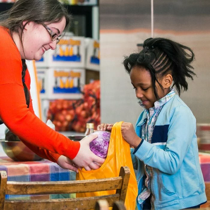 Woman helps fill the shopping bag of a young girl.