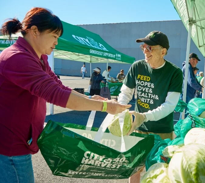 A man and woman load food into a City Harvest shopping bag