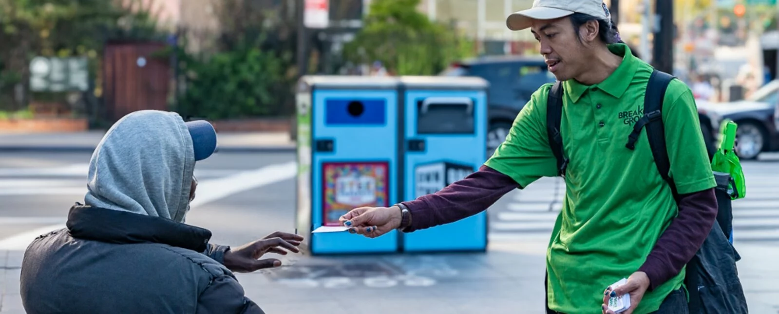 A man from Breaking Ground hands a card to a man on a bench.