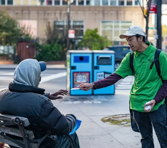 A man from Breaking Ground hands a card to a man on a bench.