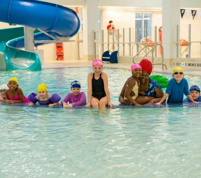 Children with bright swim caps and floaties pose in a pool at the Y.