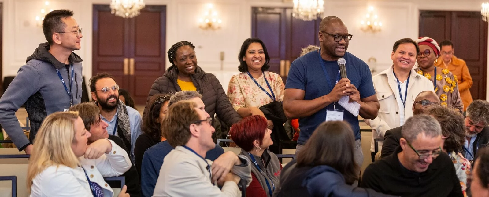 One man talks holding the microphone while others listen and smile.