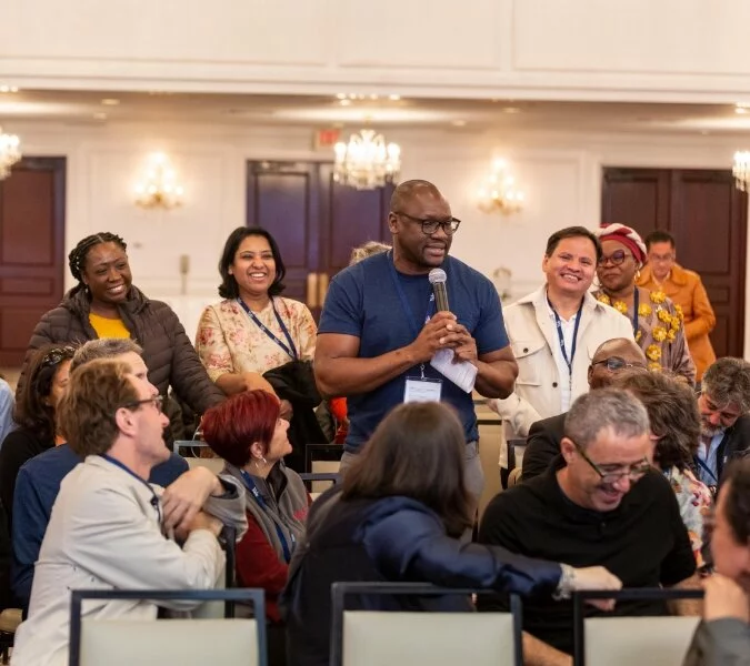 One man talks holding the microphone while others listen and smile.