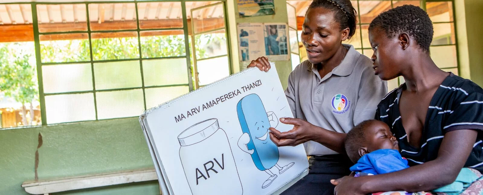 A staff member from mothers2mothers uses a visual aid to educate a mom while she holds her baby.