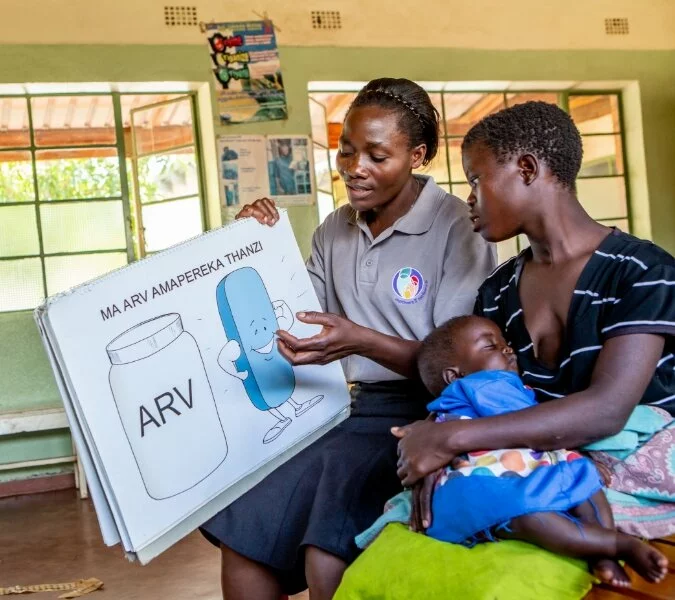 A staff member from motherstomothers uses a visual aid to educate a mom while she holds her baby.