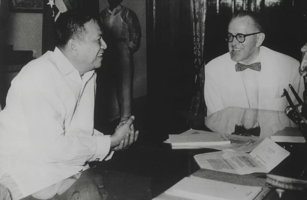 C.V. Starr and Ramon Magsayay sit together at a table talking and smiling.