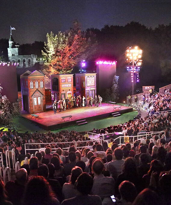 People watch Shakespeare in the Park in the evening.