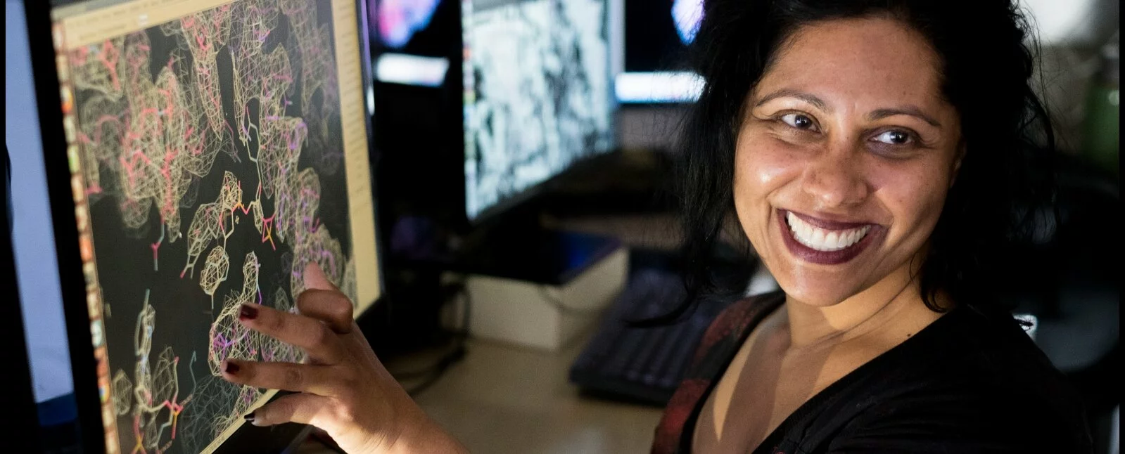 A woman working in a lab smiles while reviewing slides on a computer monitor