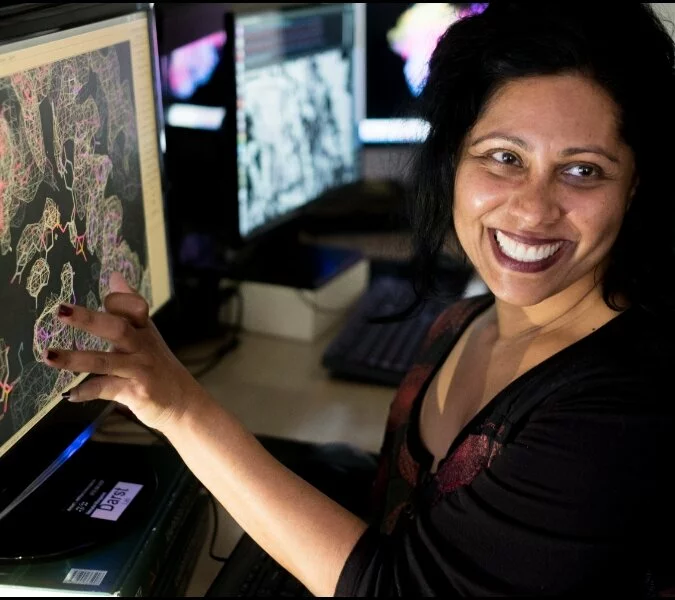 A woman working in a lab smiles while reviewing slides on a computer monitor