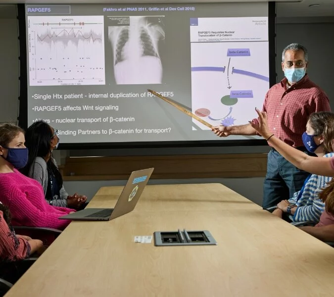 Students at Yale Medical School sit around a table discussing slides shown on a screen.